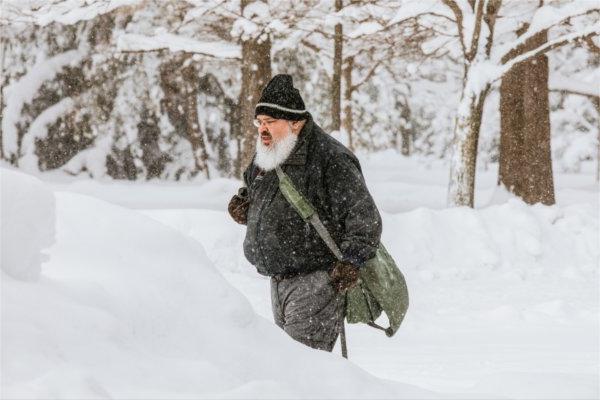  A person with a large white beard and winter hat makes their way through a wintry college campus. 
