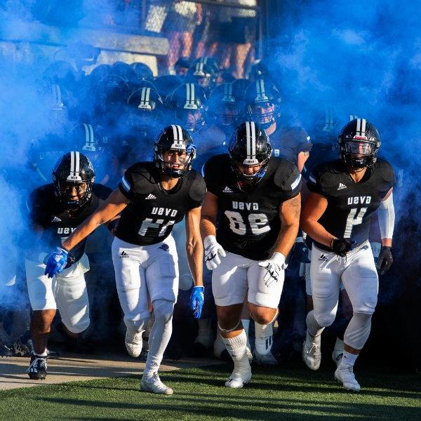 Laker football players run on to the field through cloud of blue smoke at the start of a game.